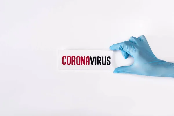 Vista superior del médico en la tarjeta de retención de guantes de látex con letras coronavirus aisladas en blanco - foto de stock