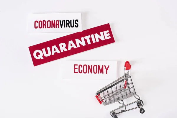 Top view of toy shopping cart near cards with quarantine, coronavirus and economy lettering on white — Stock Photo