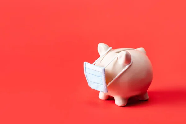 Piggy bank in small medical mask on red — Stock Photo