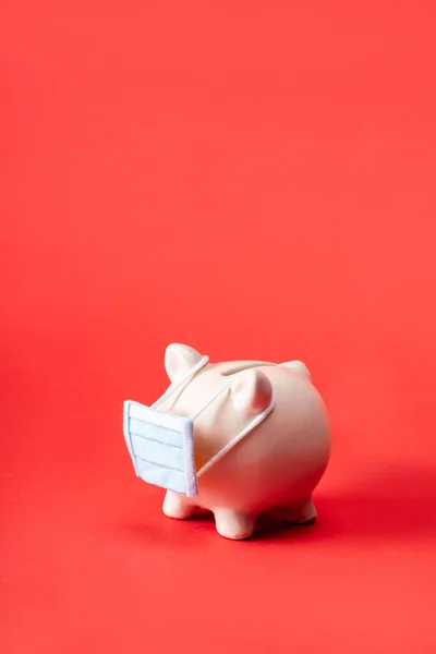 Piggy bank in small medical mask on red with copy space — Stock Photo