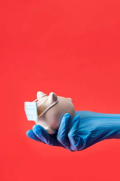 Cropped view of doctor holding piggy bank in small medical mask isolated on red — Stock Photo
