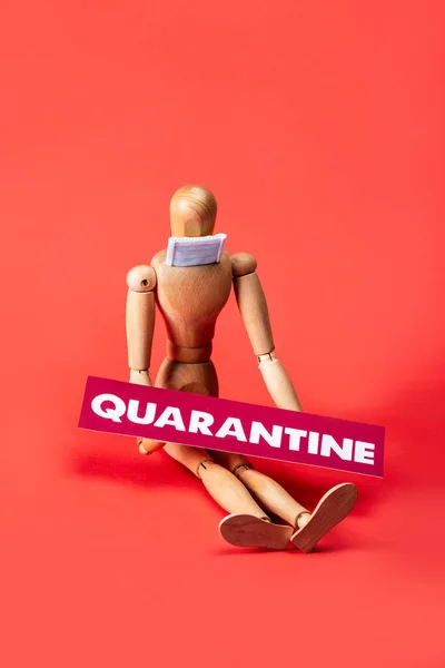 Wooden doll in small medical mask and card with quarantine lettering on red — Stock Photo