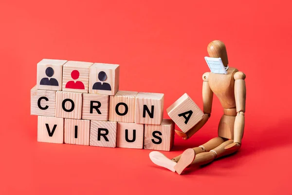 Mannequin en bois en petit masque médical près de cubes avec lettrage coronavirus sur rouge — Photo de stock