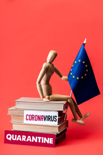 Boneca de madeira com bandeira da união europeia em livros perto de cartões com letras de quarentena e coronavírus em vermelho — Fotografia de Stock