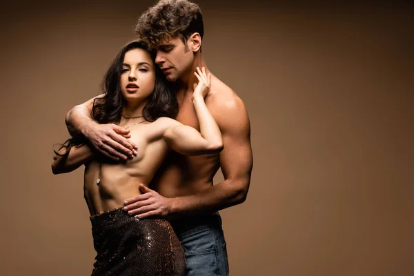 Seductive boyfriend covering breast of sexy half naked girlfriend in paillettes skirt on beige — Stock Photo