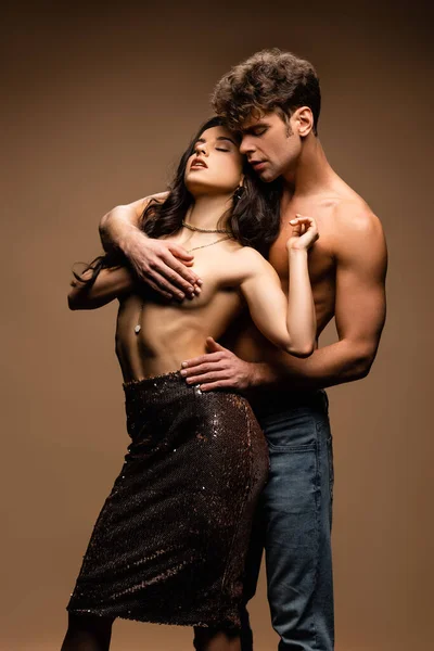 Passionate shirtless boyfriend covering breast of sexy half naked girlfriend in paillettes skirt on beige — Stock Photo