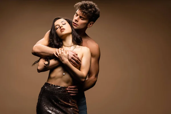 Shirtless boyfriend covering breast of passionate half naked girlfriend in paillettes skirt on beige — Stock Photo