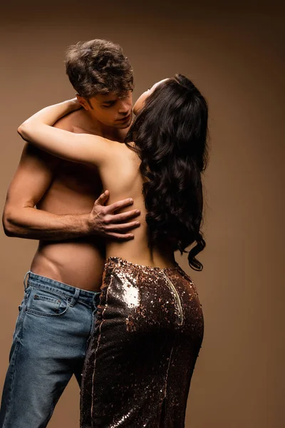 Passionate man kissing beautiful half naked girlfriend in paillettes skirt on beige — Stock Photo