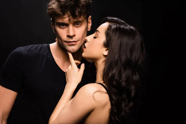 Beautiful seductive girl touching face of handsome boyfriend and going to kiss him isolated on black — Stock Photo