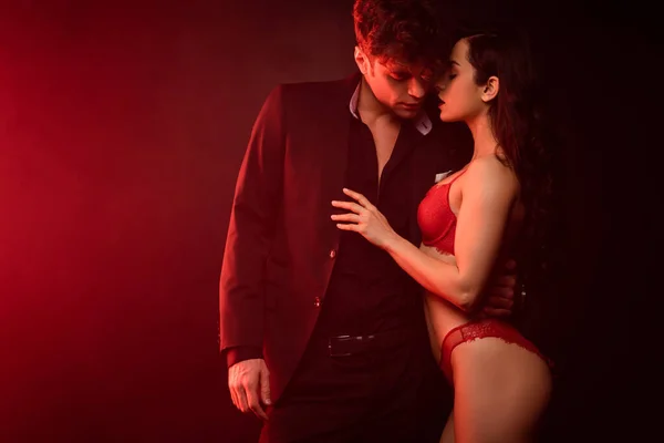 Beau couple passionné étreignant sur noir avec lumière rouge — Photo de stock