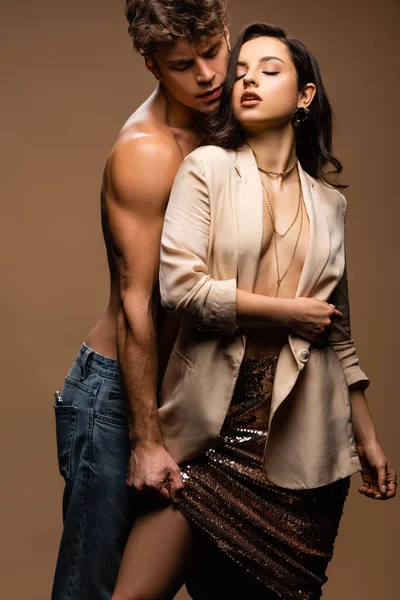 Seductive shirtless boyfriend and sexy half naked girlfriend in beige jacket isolated on beige — Stock Photo