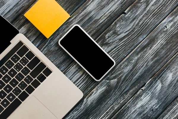 Vista dall'alto del computer portatile, smartphone con schermo bianco e note adesive sulla superficie di legno scuro — Foto stock