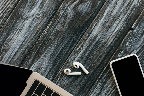 Vista dall'alto di laptop, smartphone e auricolari su una superficie di legno scuro — Foto stock