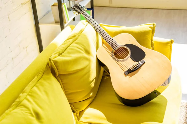 Close up of acoustic guitar on yellow sofa in sunlight — Stock Photo