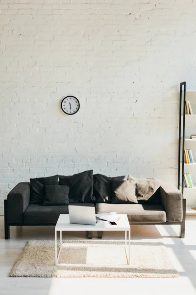 Sala de estar com sofá cinza, prateleira e mesa com laptop à luz solar — Fotografia de Stock