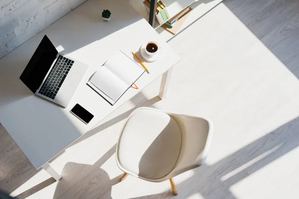 Vista superior do escritório em casa com smartphone, xícara de café e laptop na mesa à luz do sol — Fotografia de Stock