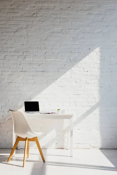 Bureau à domicile avec ordinateur portable sur la table et la chaise près de la lumière du soleil — Photo de stock