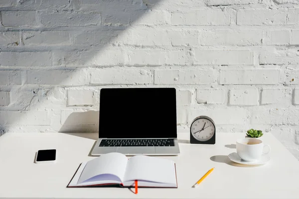 Домашний офис с ноутбуком, смартфоном, пустым блокнотом, часами и чашкой кофе при солнечном свете — стоковое фото
