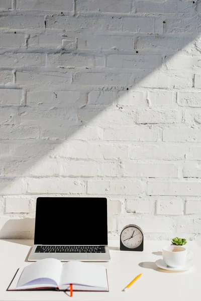 Escritório em casa com laptop, bloco de notas vazio, relógio e café à luz solar — Fotografia de Stock