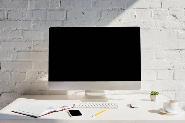 Oficina en casa con bloc de notas, taza de café, computadora y teléfono inteligente con pantallas en blanco - foto de stock