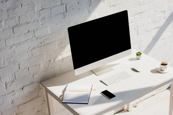 Домашний офис с блокнотом, кофейной чашкой, компьютером и смартфоном с пустыми экранами — стоковое фото