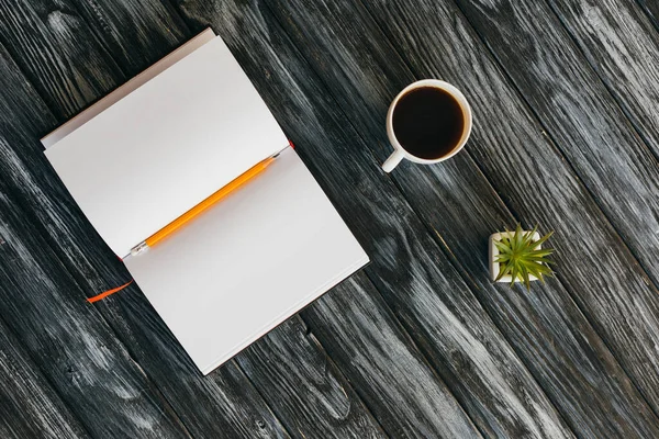 Vue du dessus du bloc-notes vide, crayon, tasse de café et succulent sur une surface en bois sombre — Photo de stock