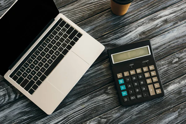 Vista superior da calculadora, café para ir e laptop com tela em branco na superfície de madeira escura — Fotografia de Stock