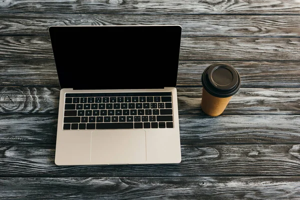 Draufsicht auf Laptop mit leerem Bildschirm und Kaffee zum Mitnehmen auf dunkler Holzoberfläche — Stockfoto