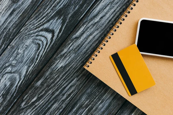 Vista superior do bloco de notas, cartão de crédito e smartphone com tela em branco na superfície de madeira escura — Fotografia de Stock