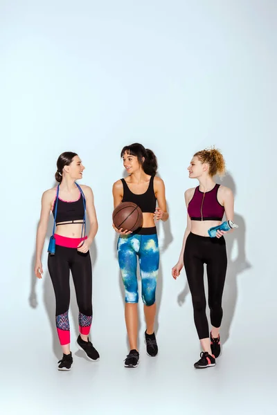 Feliz africana americana chica celebración de baloncesto y caminar con deportivo mujeres en blanco - foto de stock