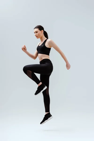 Attraktive Frau in schwarzer Sportbekleidung springt auf Weiß — Stockfoto