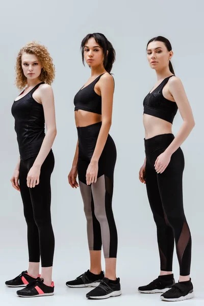 Mulheres atraentes e multiculturais em sportswear de pé isolado em branco — Fotografia de Stock