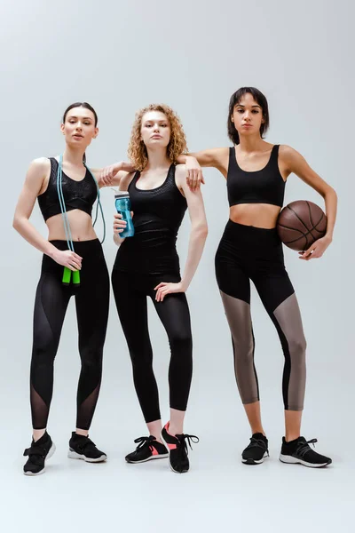 Sportive and multicultural girls standing with sport equipment on white — Stock Photo