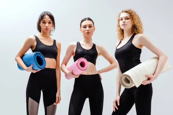 Mujeres deportivas y multiculturales que sostienen alfombras de fitness en blanco - foto de stock