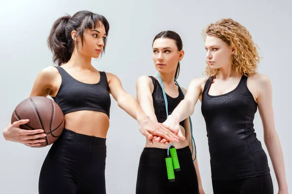 Attractive multicultural girls in sportswear putting hands together on white — Stock Photo