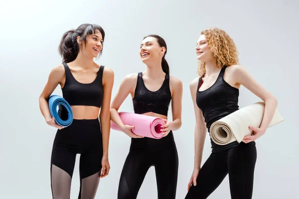 Mulheres felizes e multiculturais segurando tapetes de fitness em branco — Fotografia de Stock
