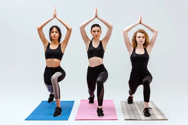 Mulheres atraentes e multiculturais exercitando-se em tapetes fitness isolados em branco — Fotografia de Stock