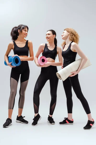 Cheerful and multicultural women holding fitness mats on white — Stock Photo