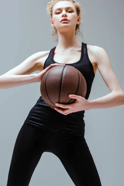 Кучерява жінка в спортивному одязі тримає баскетбол ізольовано на сірому — стокове фото