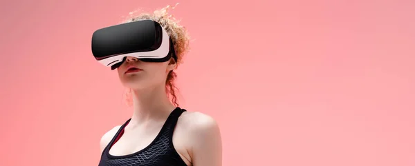 Prise de vue panoramique de la femme en vêtements de sport et casque de réalité virtuelle sur rose — Photo de stock