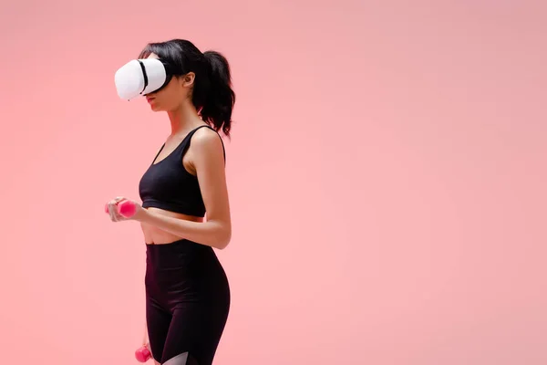 African american sportswoman in virtual reality headset exercising with dumbbells on pink — Stock Photo