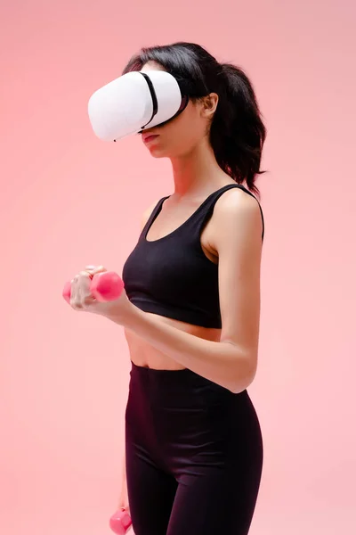 African american girl in sportswear and virtual reality headset exercising with dumbbells on pink — Stock Photo