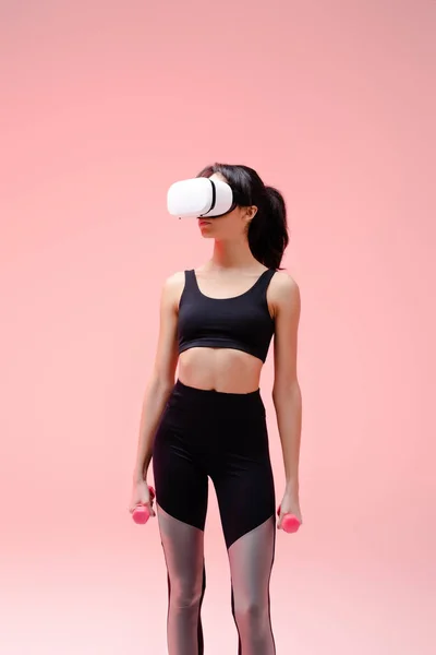 African american woman in sportswear and virtual reality headset exercising with dumbbells on pink — Stock Photo