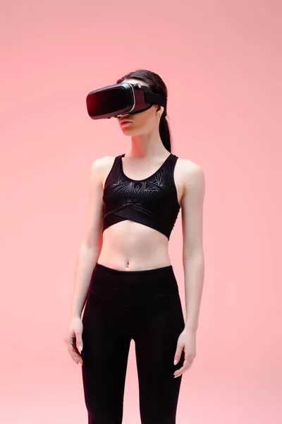 Спортсменка в наушниках виртуальной реальности, стоящая на розовом — стоковое фото