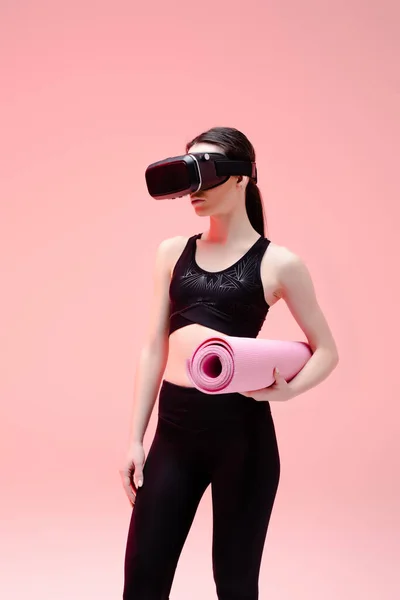 Sportlerin im Virtual-Reality-Headset hält Fitnessmatte auf rosa — Stockfoto