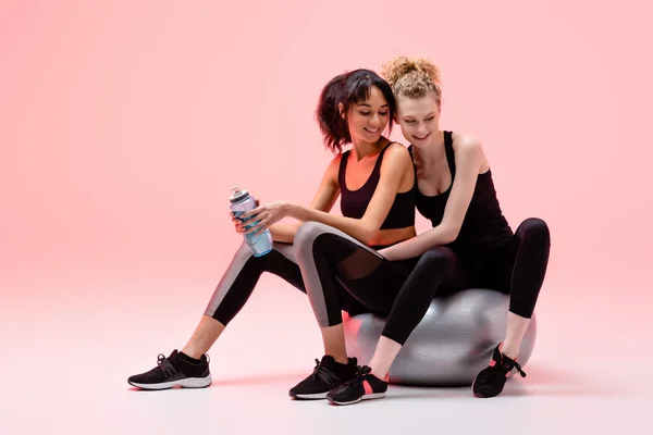 Chica feliz sentada en el centro comercial de fitness con la mujer americana africana alegre en rosa - foto de stock