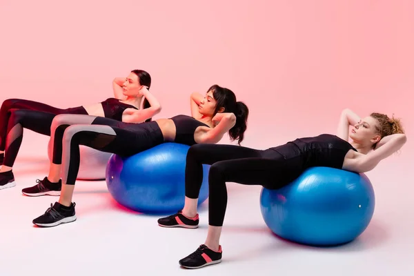 Multicultural girls exercising on fitness balls on pink — Stock Photo