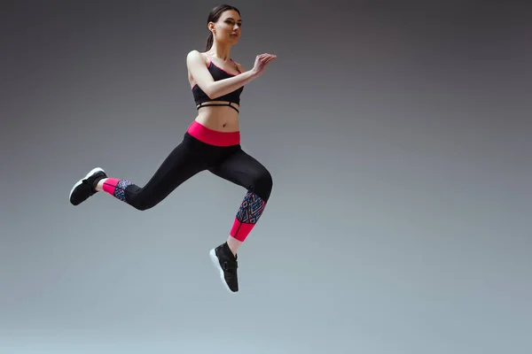 Красива жінка в спортивному одязі стрибає на сірому — стокове фото