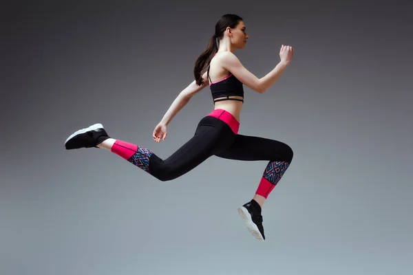 Вид збоку красива жінка в спортивному одязі, стрибає на сірому — стокове фото