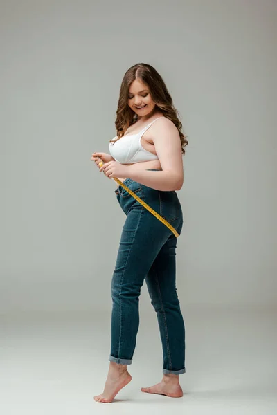 Alegre más tamaño mujer en jeans y sujetador cuerpo de medición en gris - foto de stock